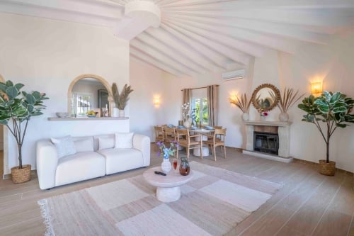 Woonkamer met witte bank, eettafel en open haard onder gewelfd plafond